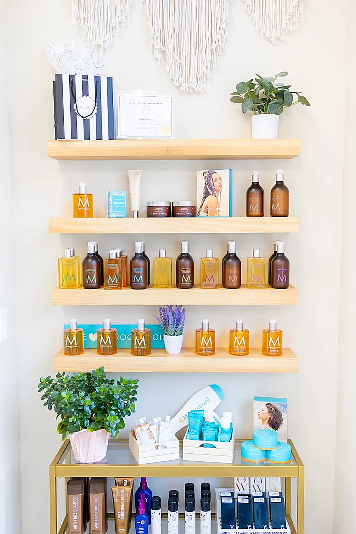 Retail shelf of Moroccanoil hair products with a plant and macrame wall hanging